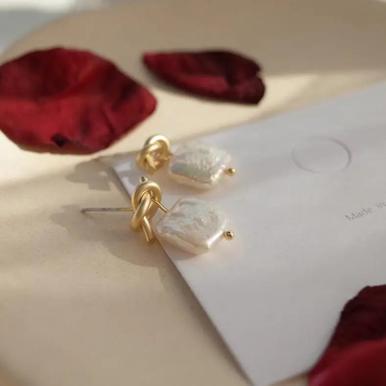 Side close-up of Bound in Grace Earrings showing the 925 silver needle and detailed gold knot with pearl drop on a neutral background.