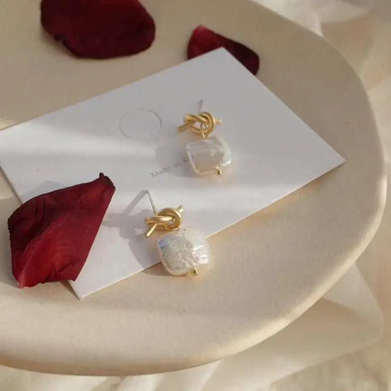 Angled view of Bound in Grace Earrings on a card, highlighting the textured pearl drop and gold knot stud in natural light.