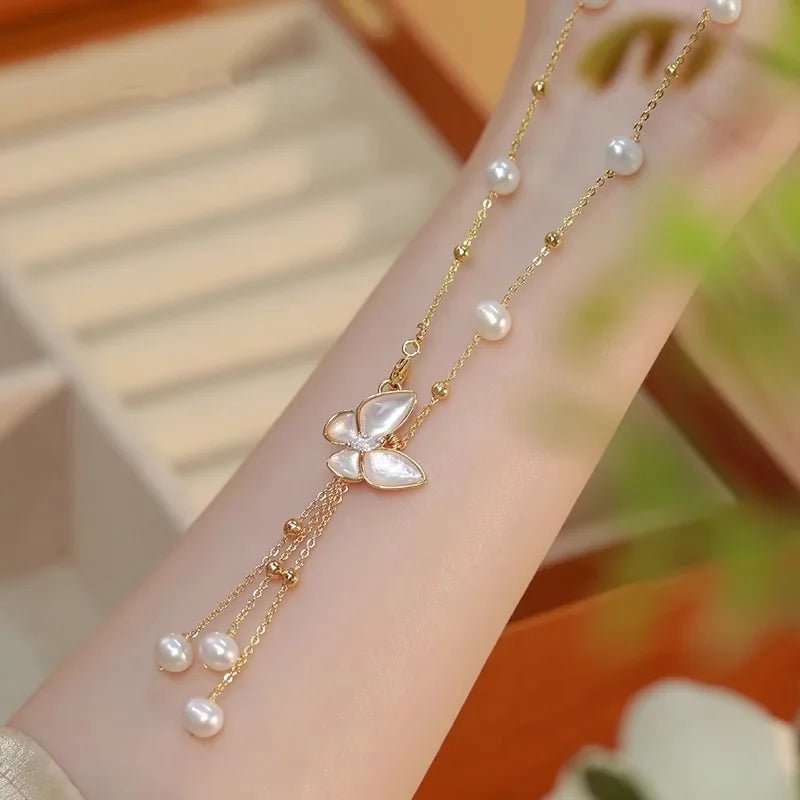 Wings of Love Necklace draped on wrist, highlighting butterfly charm and freshwater pearls on gold-filled chain for soft, romantic style.