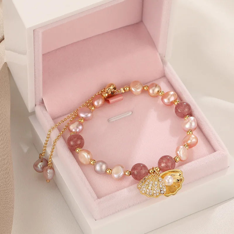Pink Whisper Shell Bracelet displayed in a pink velvet jewelry box, featuring pearls, quartz beads, and a gold shell charm.