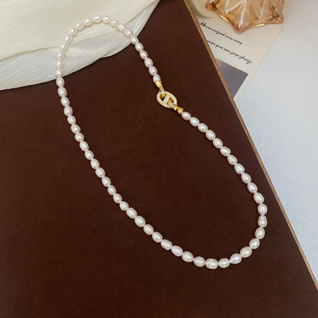 Stylish Heavenly Glow Choker made of freshwater pearls and a gold crystal cross clasp, arranged diagonally on a brown surface.