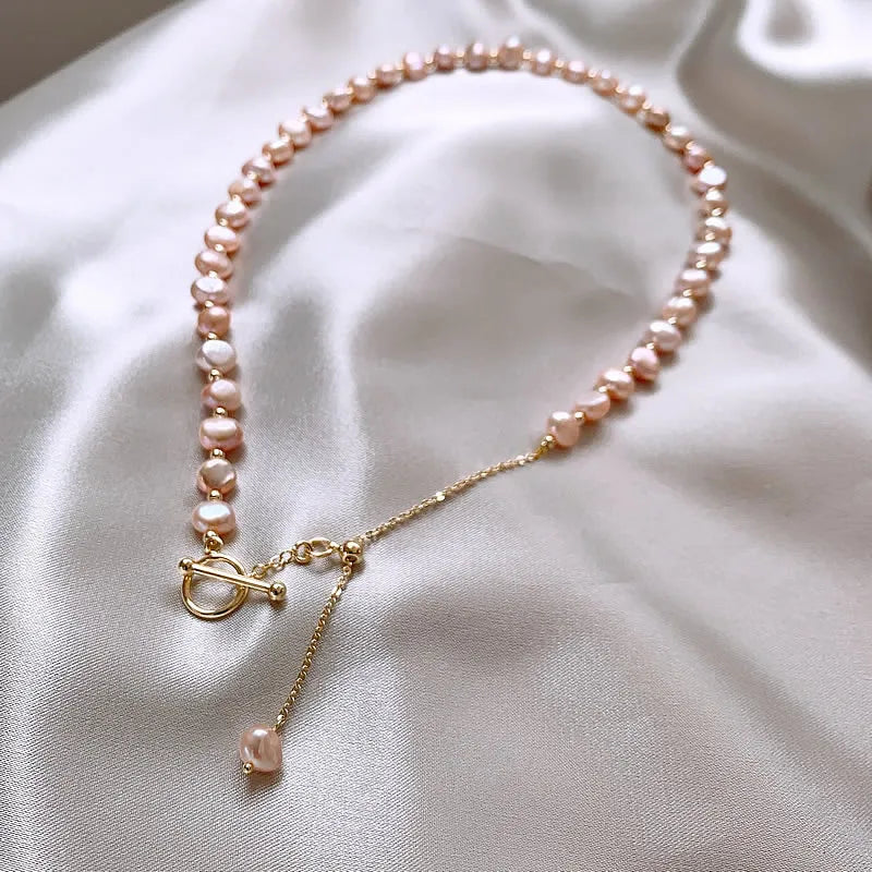 Pink Baroque Pearl Gold-Filled Necklace laid flat with asymmetrical pearls and a dangling gold chain on a satin surface.
