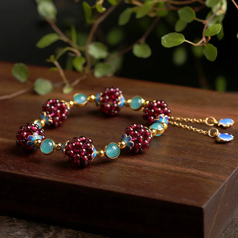 Aurora Stone Bracelet on a wooden surface, featuring rich garnet beads, aqua amazonite, and gold-filled chain with blue charms.