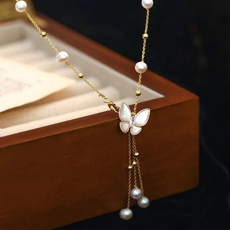 Wings of Love Necklace displayed on wooden box, featuring butterfly charm and pearl drops on 14K gold-filled chain for timeless elegance.