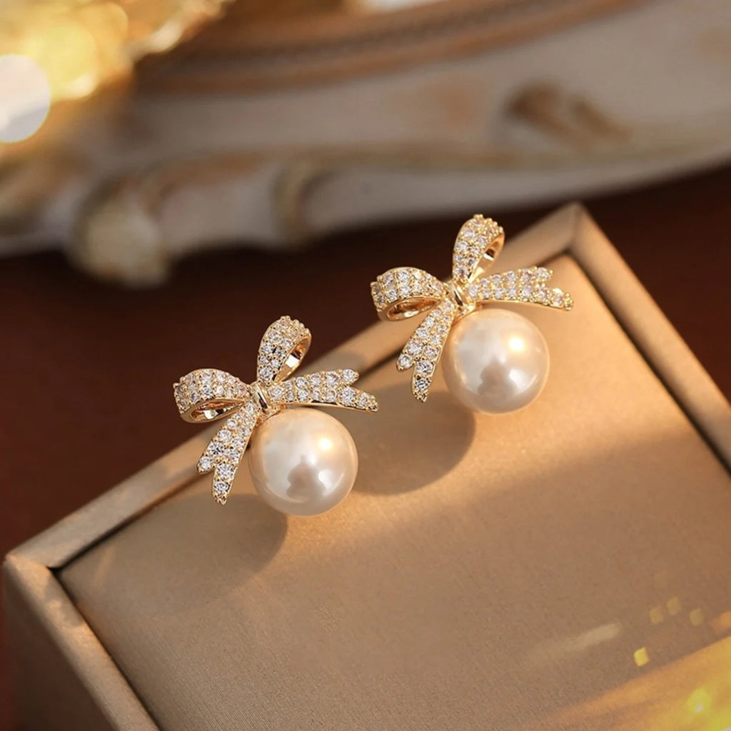 Silver Bow Diamond & Pearl Stud Earrings featuring a sparkling bow design with a large pearl drop, displayed on a gift box for elegant presentation.