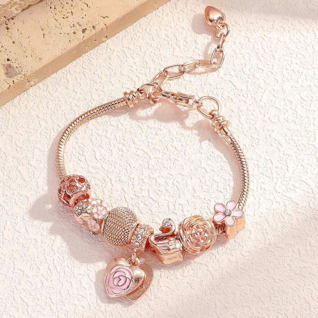 Rosette Swan Charm Bracelet with pink enamel rose heart charm and swan detail, laid flat on a stone surface under natural light.