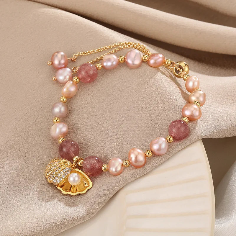 Pink Whisper Shell Bracelet with pink freshwater pearls, strawberry quartz, and gold shell charm on beige fabric background.
