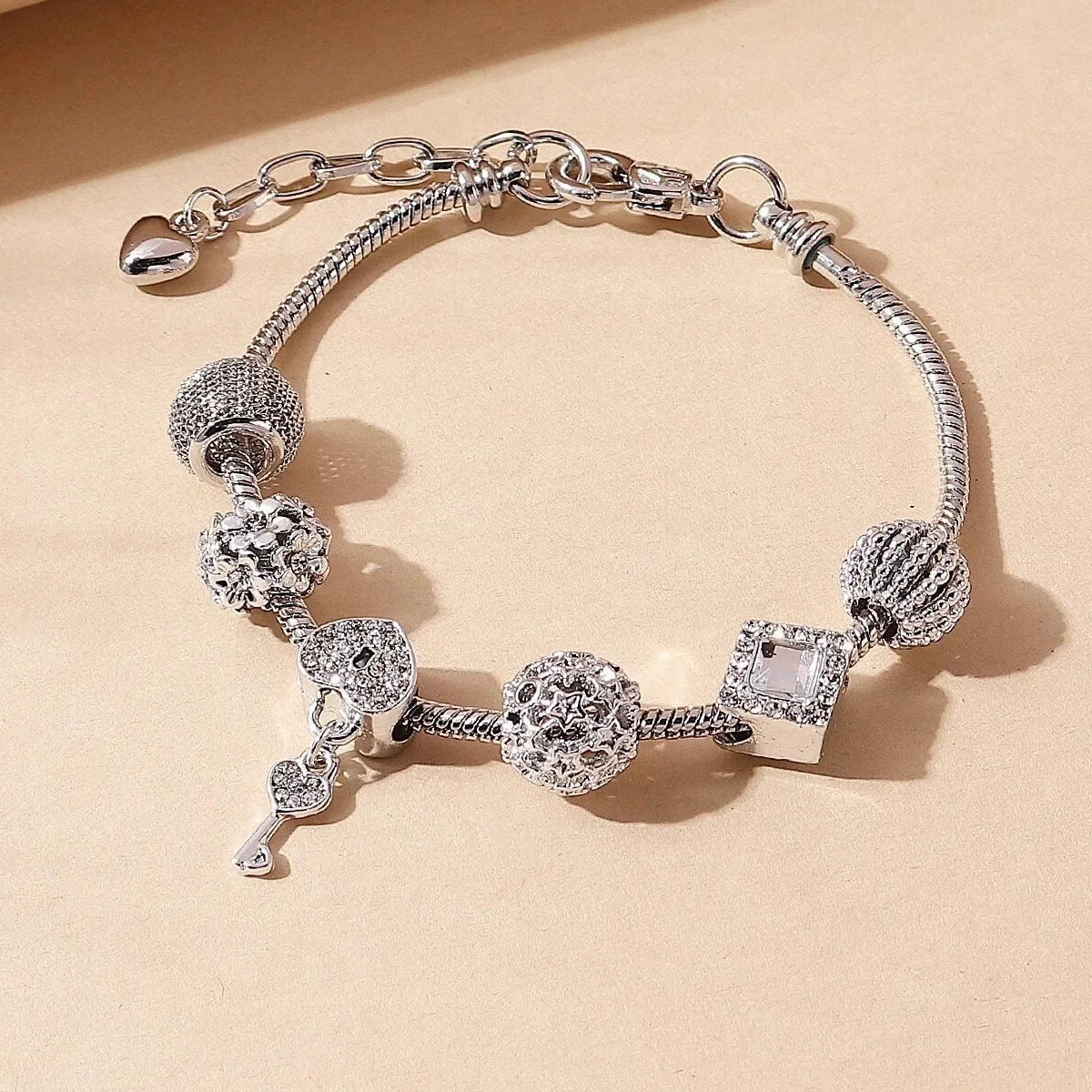 Silver-tone charm bracelet with crystal and textured beads, including a key and square charm, ideal for stylish accessorizing.