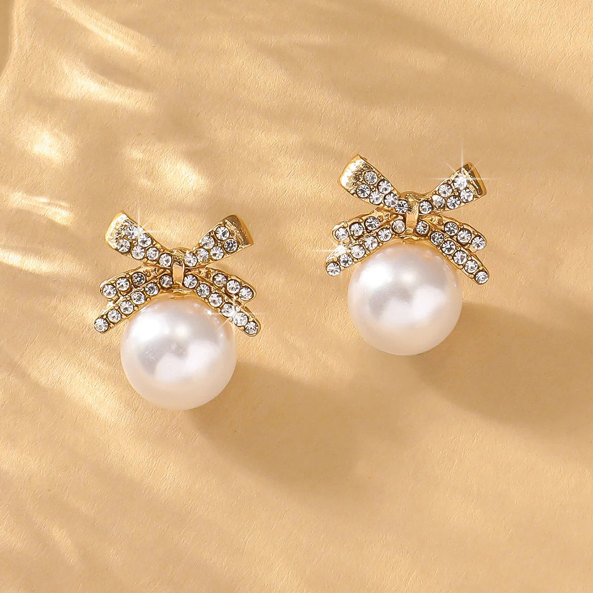 Pair of Silver Bow Diamond & Pearl Stud Earrings on satin surface, emphasizing the intricate diamond-studded bow and glossy pearl drop.