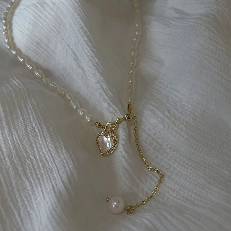 Pearl of My Heart Necklace laid on white fabric, featuring a heart-shaped charm and pearl drop on a gold chain for a soft, romantic appeal.