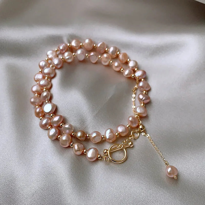 Coiled Pink Baroque Pearl Gold-Filled Necklace showcasing irregular pearls and a dangling gold chain accent on satin background.