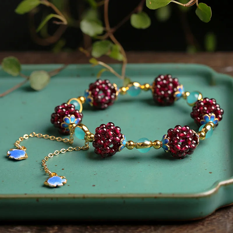 Aurora Stone Bracelet displayed on a green tray, showcasing garnet clusters, amazonite stones, and gold-filled chain with blue charms.