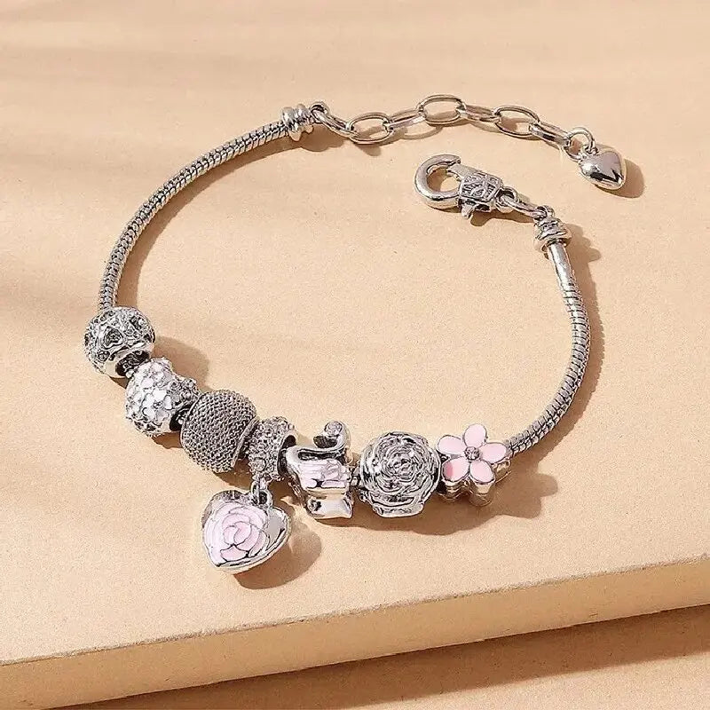 Rosette Swan Charm Bracelet in silver with pink enamel charms including a swan, rose, and heart, styled on a neutral background.
