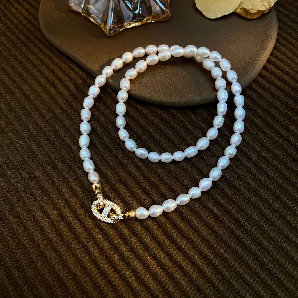 Heavenly Glow Choker with freshwater pearls and a crystal-studded gold cross clasp, displayed on a textured brown surface.