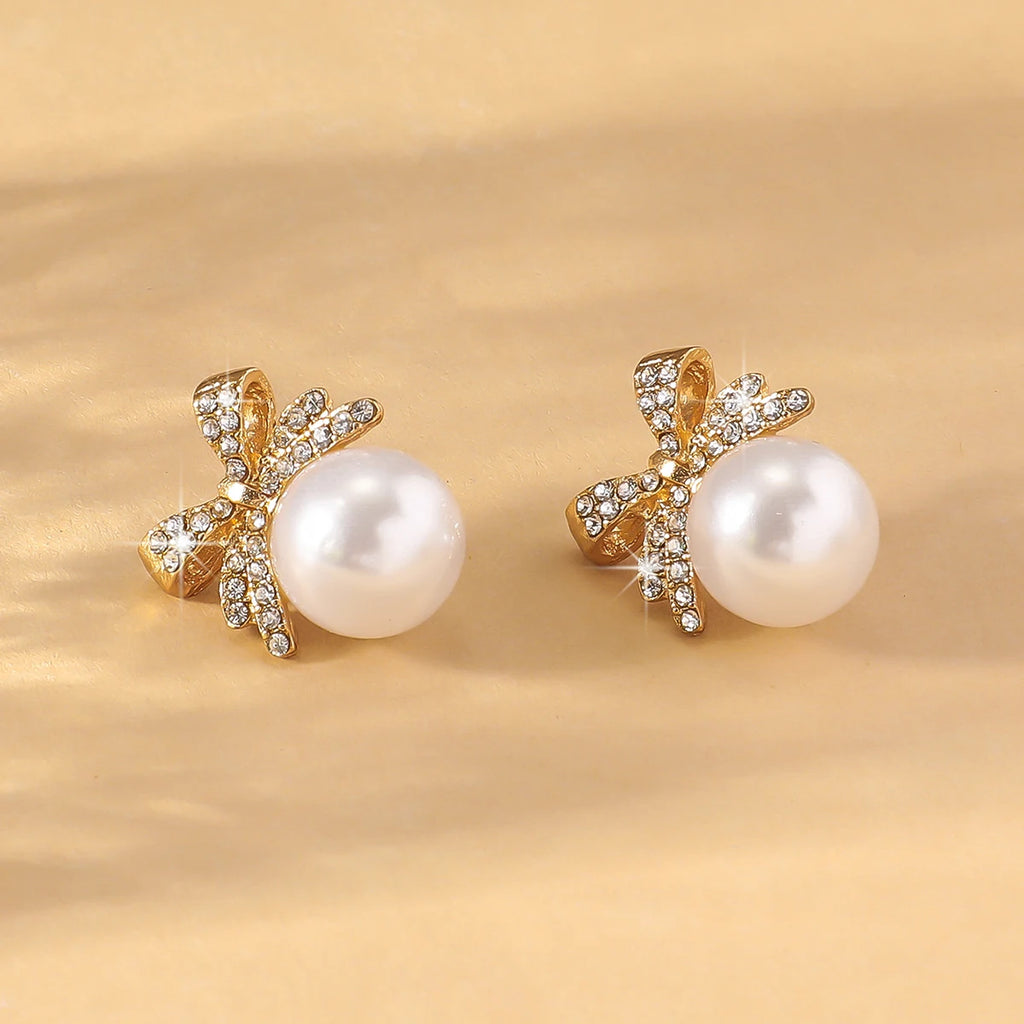 Close-up of Silver Bow Diamond & Pearl Stud Earrings on beige background, highlighting the shimmering bow and lustrous pearl centerpiece.