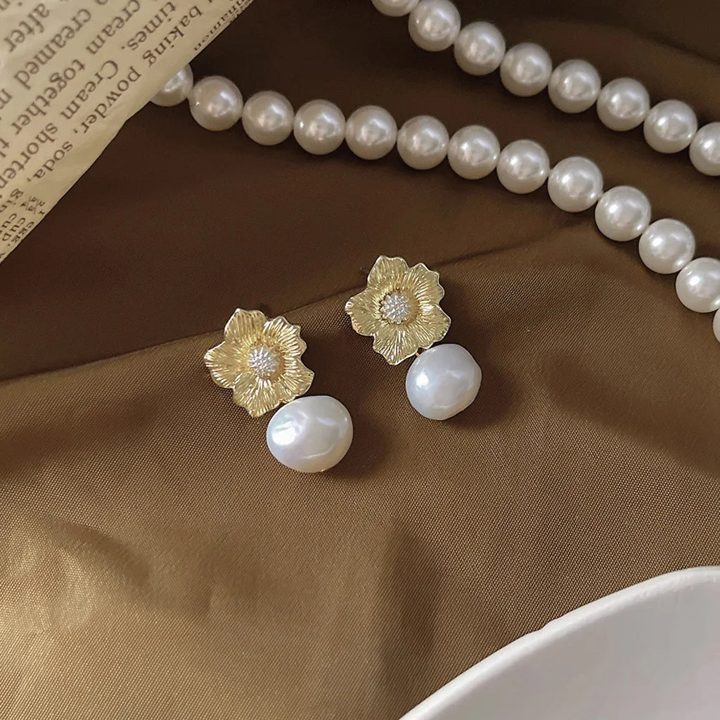 Delicate Pearl Pixie Studs with textured gold floral studs and lustrous baroque pearl drops, styled on a satin background with pearl necklace.