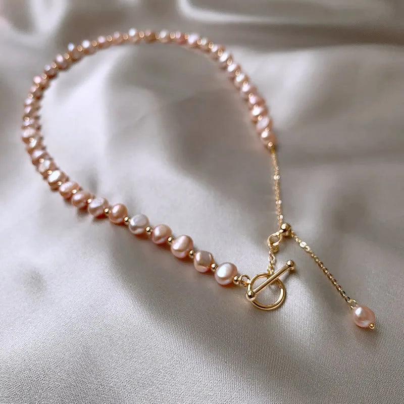 Asymmetrical Pink Baroque Pearl Gold-Filled Necklace with gold toggle clasp and pearl drop chain on a silky surface.