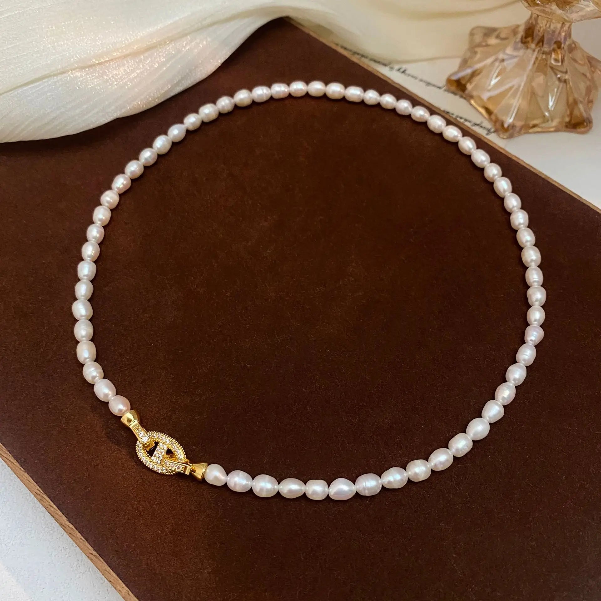 Heavenly Glow Choker necklace with natural pearls and a sparkling gold cross clasp, laid flat on a dark velvet background.